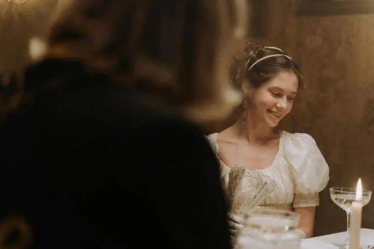 A smiling woman in a vintage white dress enjoys a candlelit dinner with an elegant ambiance.