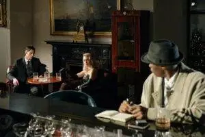 A detective watches a conversation unfold in a vintage lounge, capturing the essence of noir fiction.