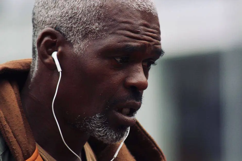 Close-up portrait of an African American man with grey hair wearing earphones, captured in a side view outdoors in New York.