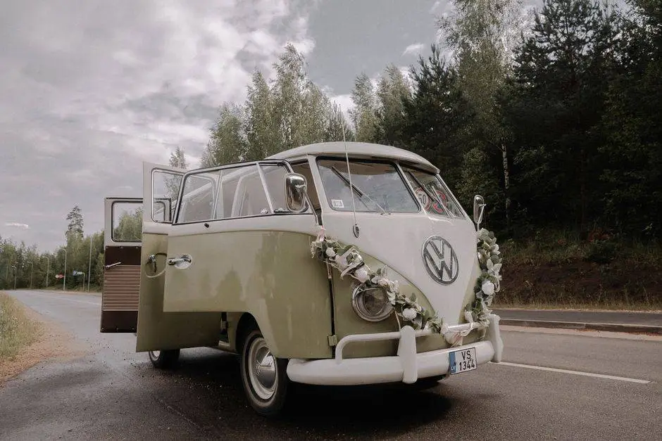 A vintage Volkswagen van adorned with flowers parked on a scenic road, surrounded by nature.
