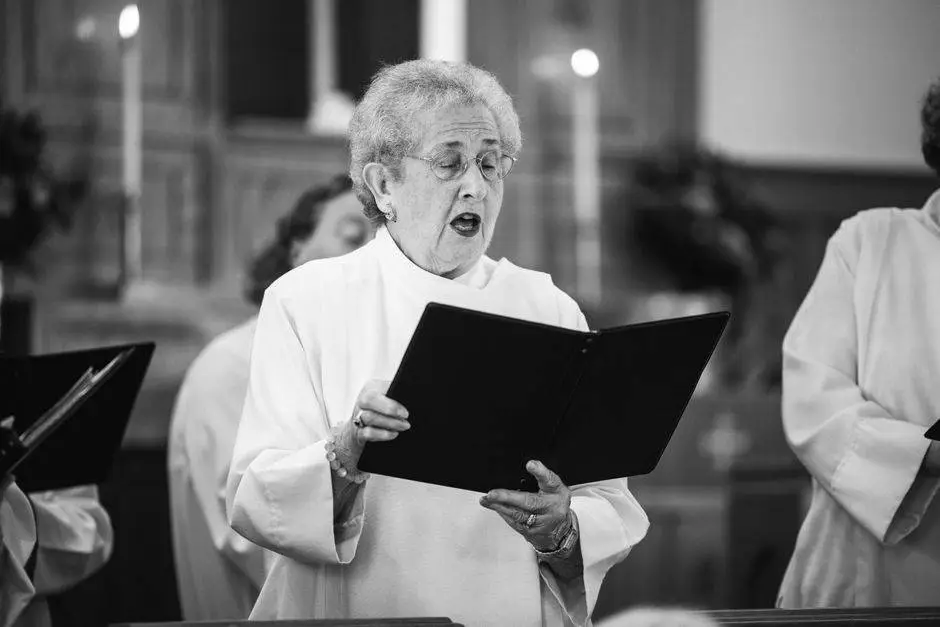 An elderly woman sings in a church choir, emphasizing tradition and spiritual performance.