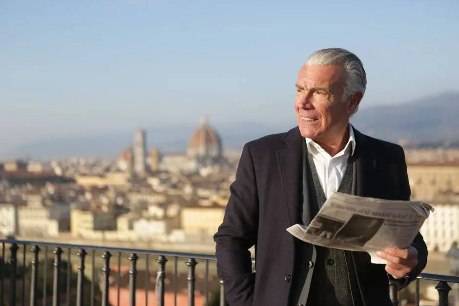 Elderly man reads newspaper on balcony overlooking Florence. Clear day with iconic architecture.