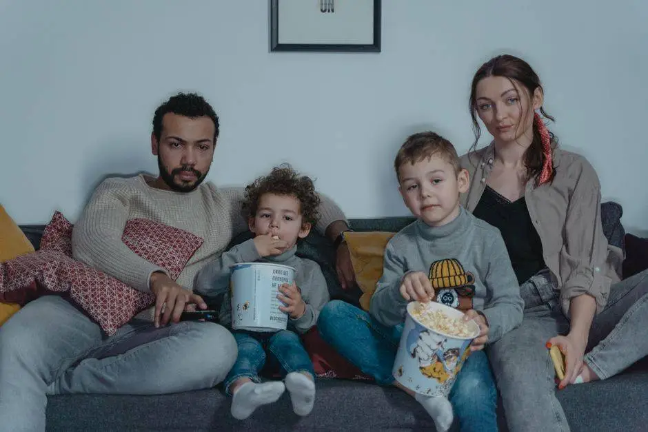 Family of four enjoying a cozy movie night with popcorn on the sofa.