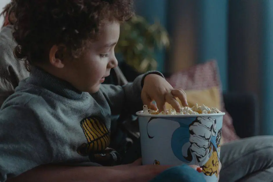 A young child enjoys a bowl of popcorn while sitting indoors.