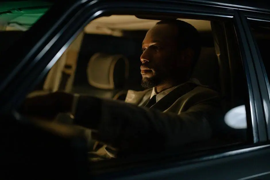 A focused man driving at night, illuminated by dim interior car lights.