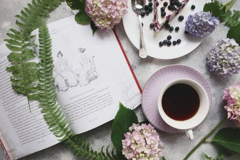 Aesthetic flat lay featuring a book, coffee, hydrangeas, and blueberry dessert.